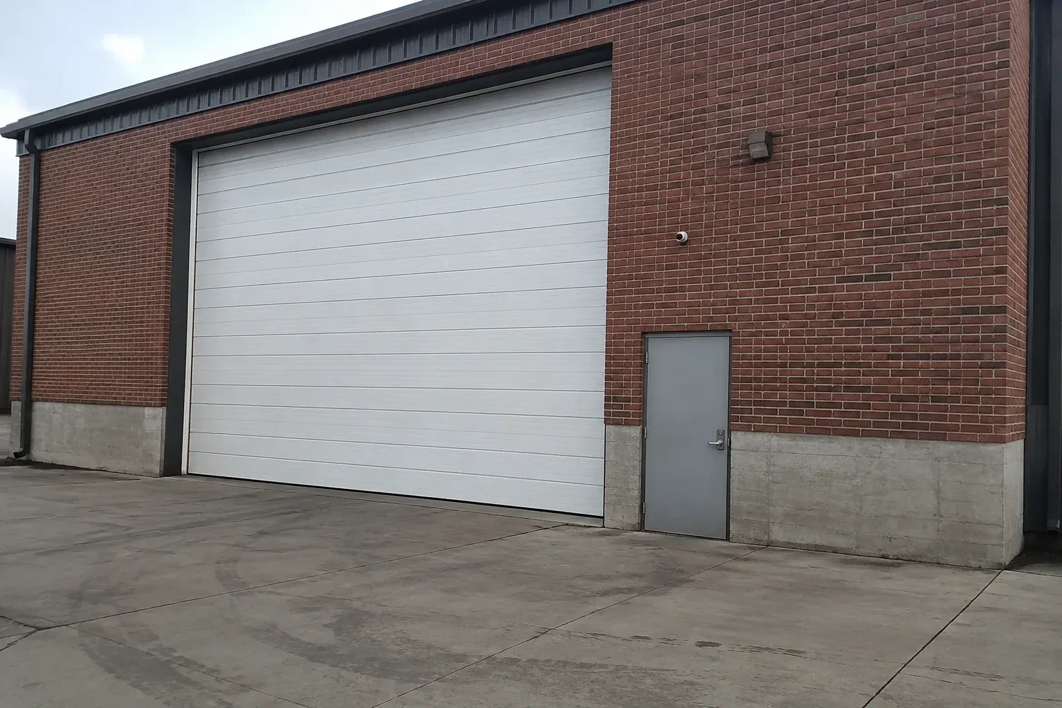 Tall closed sectional loading door beside a personnel door at a brick unit. — Commercial Sectional Door Repair, Oshawa